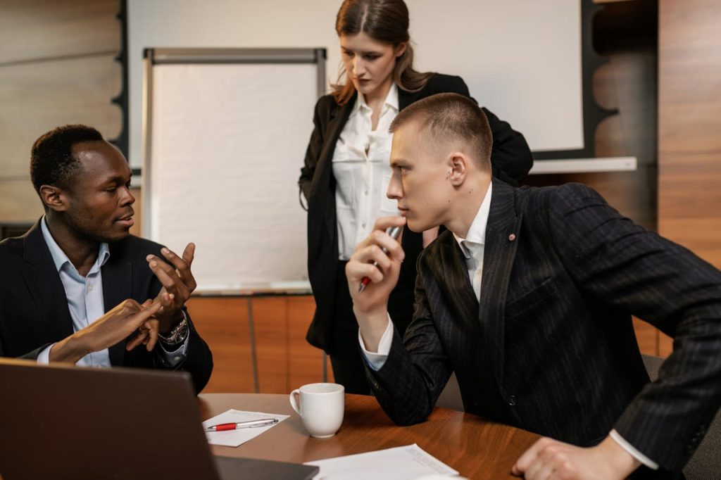 a-people-talking-together-in-the-office-8134160 Diverse colleagues in active discussion around a conference table in a modern office setting.